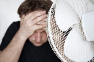 man cooling off in front of electric fan
